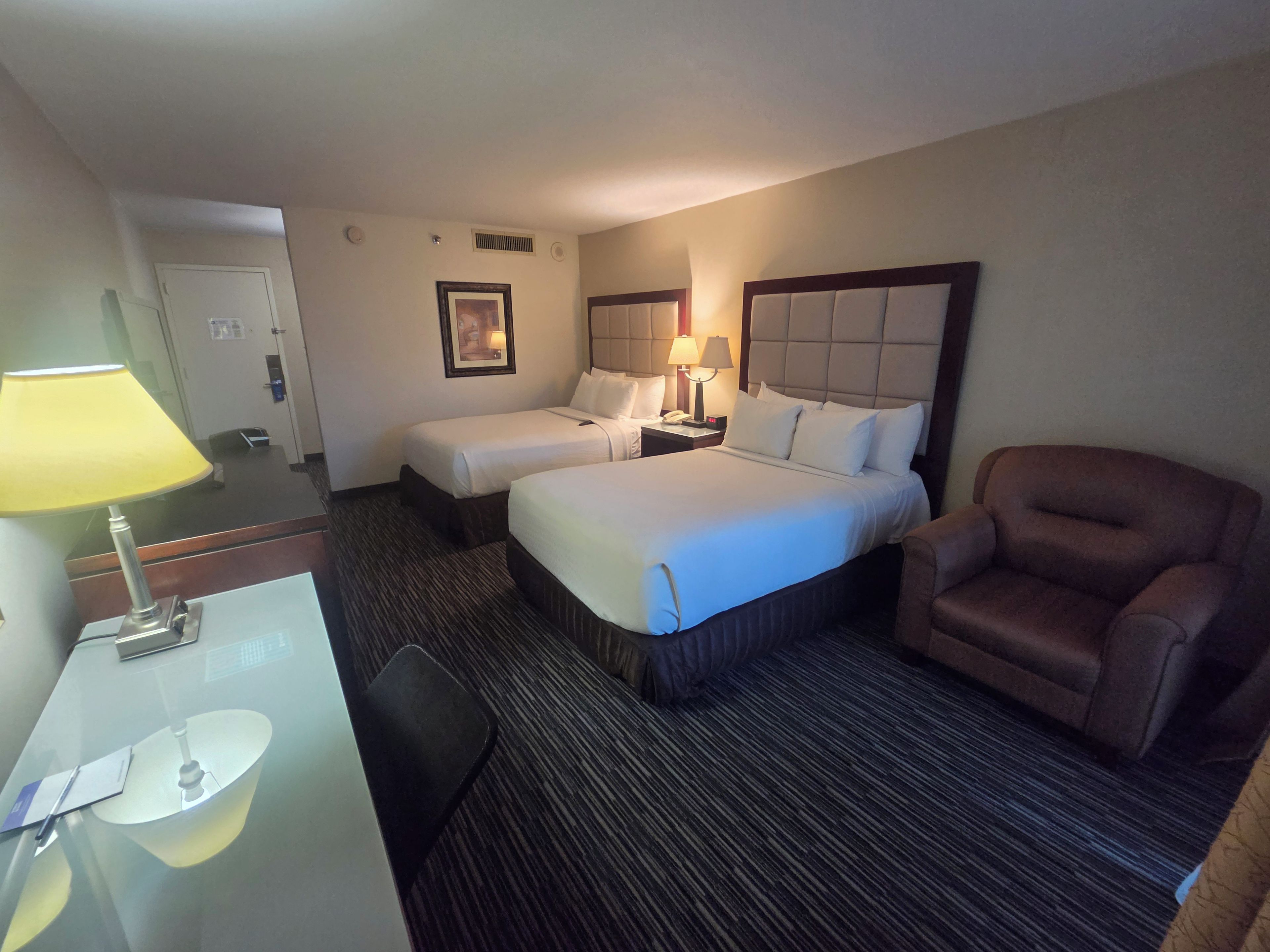 A hotel room with two beds, a desk with a lamp, a chair, and a bedside table with a phone.