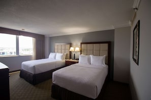 A hotel room with two beds, a nightstand with lamps, a window with curtains, and a framed picture on the wall.