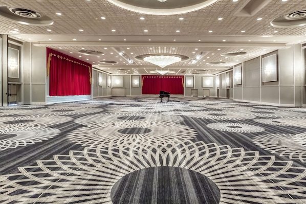 Un amplio salón con alfombra estampada, un telón rojo de fondo y una gran lámpara de araña.