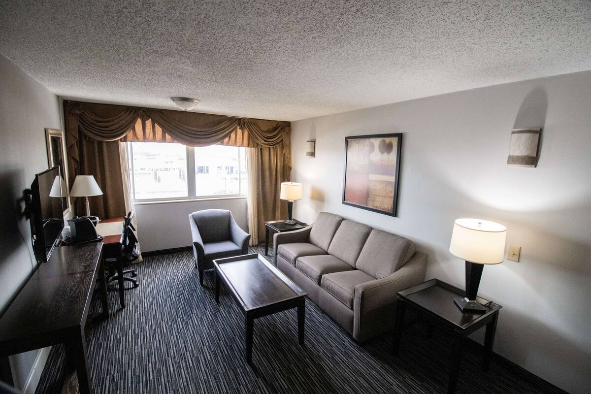 Een hotelkamer met een bank, fauteuil, bureau en lampen.