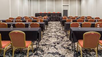 A conference room with rows of tables and chairs, a patterned carpet, and a stage with a curtain.
