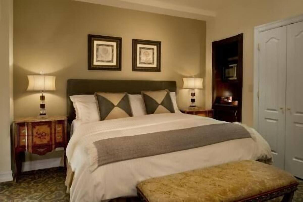 A neatly arranged hotel room with a bed, two bedside lamps, a bench, and a door.