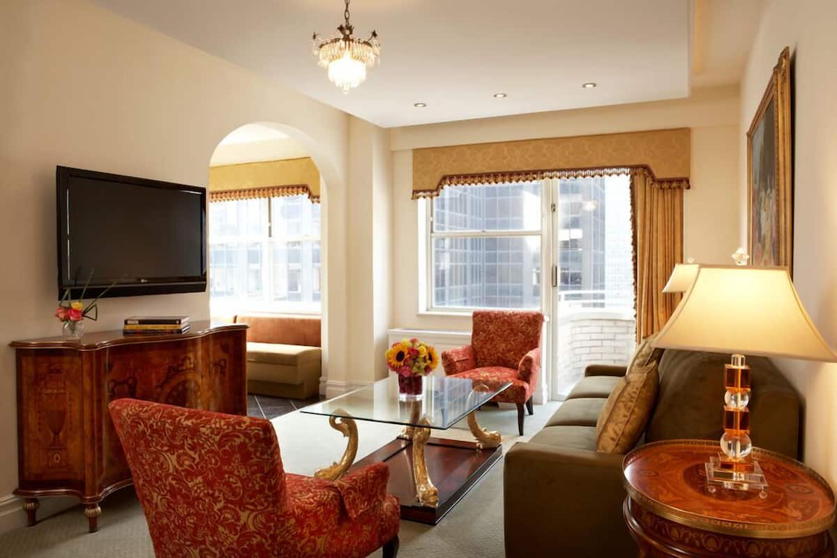 A living room with a glass coffee table, red patterned chairs, a sofa, a television, and a lamp.