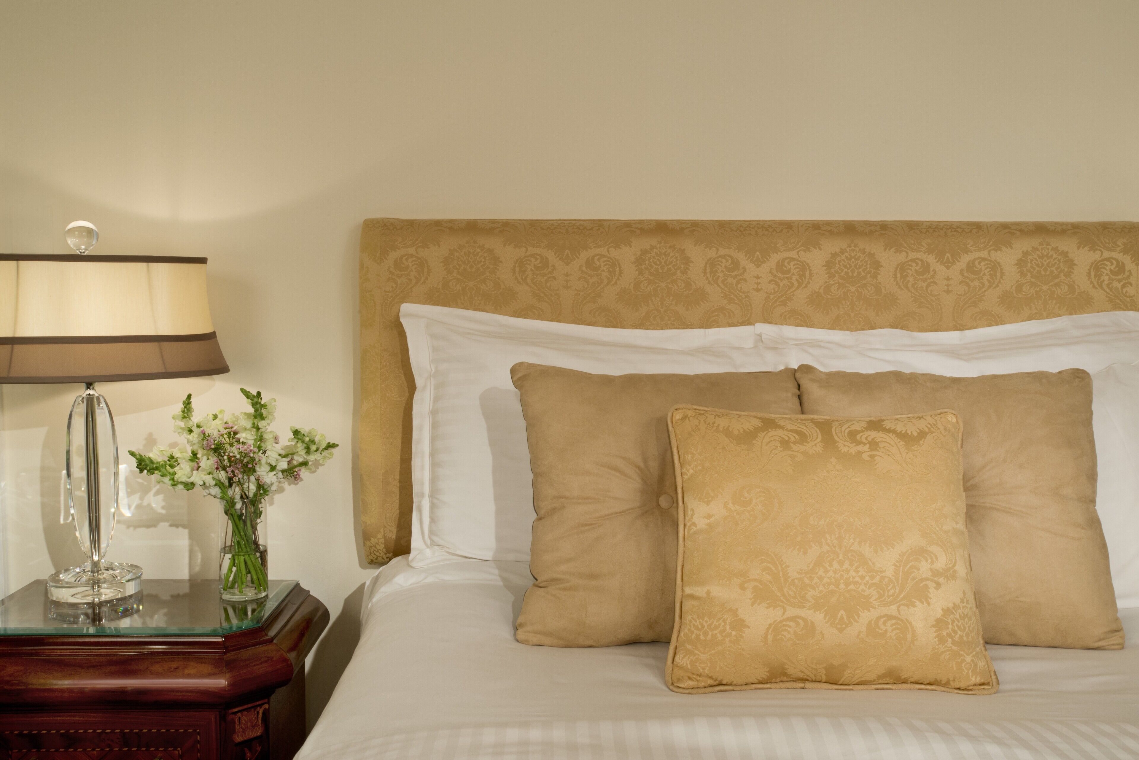 Un letto rifatto con una testiera decorata, un comodino con una lampada e un vaso con fiori.