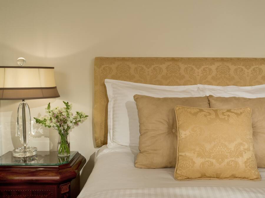 Un letto rifatto con una testiera decorata, un comodino con una lampada e un vaso con fiori.