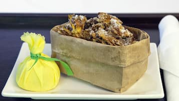 A food basket with a paper bag containing fried items, a yellow mesh bag with a green ribbon, and a white plate on a dark wooden table.