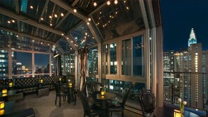 A rooftop bar with a glass ceiling, city views, and modern furnishings.