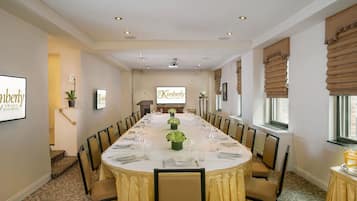 Un salón de conferencias con una larga mesa dispuesta para una reunión, equipado con sillas, un atril y una pantalla que muestra 'The Kimberly'.