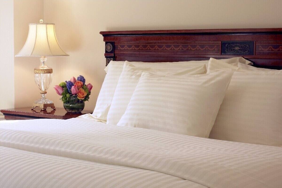 A neatly made bed with white linens, a wooden headboard, and a bedside table with a lamp and a vase of flowers.