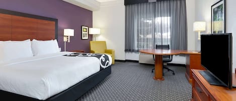 A hotel room with a large bed, a desk with a chair, a television, and a window with curtains.