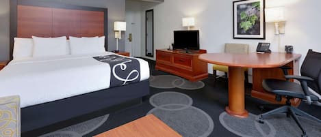 A hotel room with a large bed, a desk with a chair, a television, and a small table.