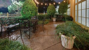 Un patio al aire libre con una mesa y sillas, rodeado de plantas en macetas y una valla de madera.