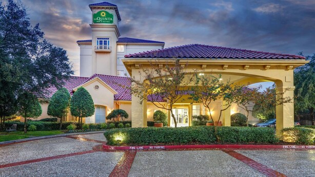 Un hotel con una torre destacada, un acceso cubierto y un jardín cuidado.