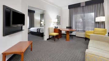 Habitación de hotel con televisión, cama, escritorio, silla, sofá y ventana con cortinas.