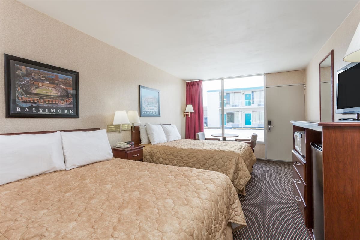 A hotel room with two beds, a television, a desk, and a window with a view of buildings.