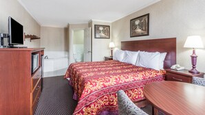 A hotel room with a large bed, a desk, a chair, a TV, a lamp, and a bathroom. - Ramada Limited Norfolk (Norfolk)