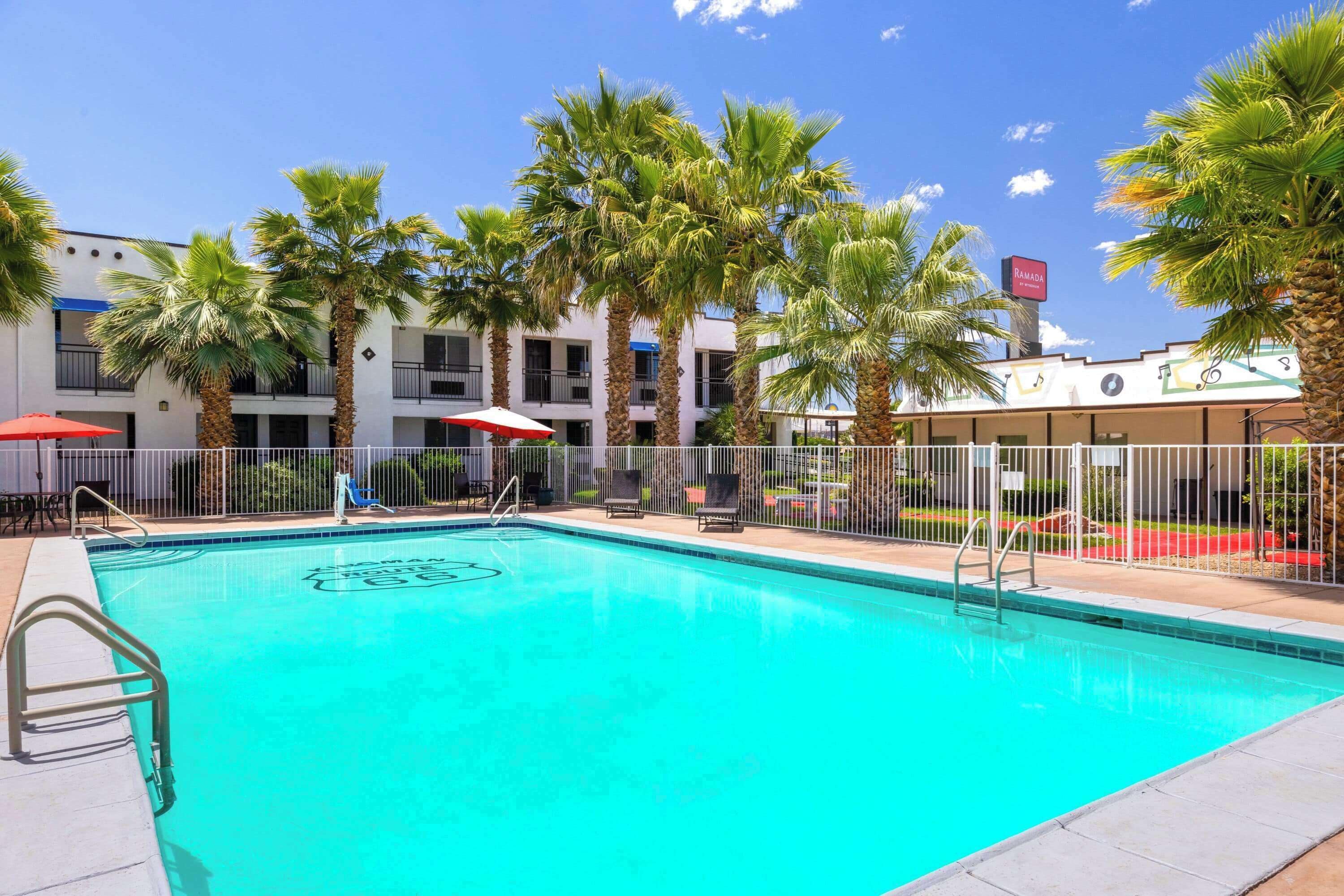 A swimming pool with a palm tree-lined deck, a sign indicating Ramadan, and a building with balconies.