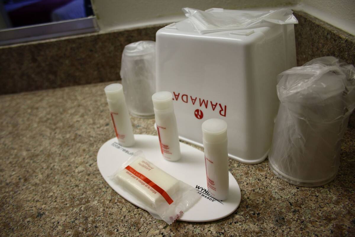 Ein Badezimmer-Waschtisch mit einer weißen Ablage, auf der sich verschiedene Pflegeprodukte, eine weiße Flasche mit roter Schrift und ein weißer Behälter mit roter Schrift befinden.