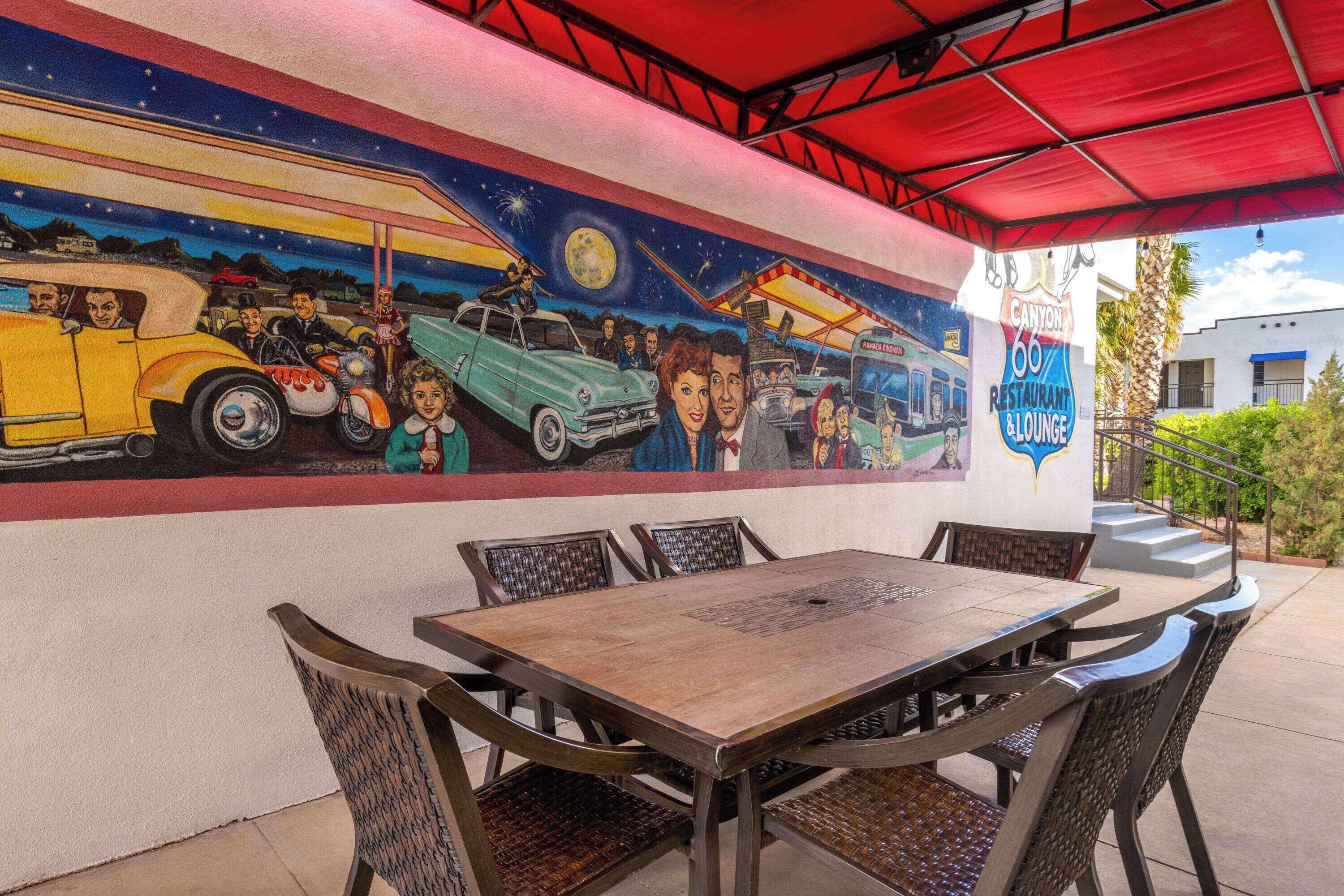 Une fresque représentant une scène avec une voiture ancienne, une table et des chaises, le tout sous un auvent rouge.