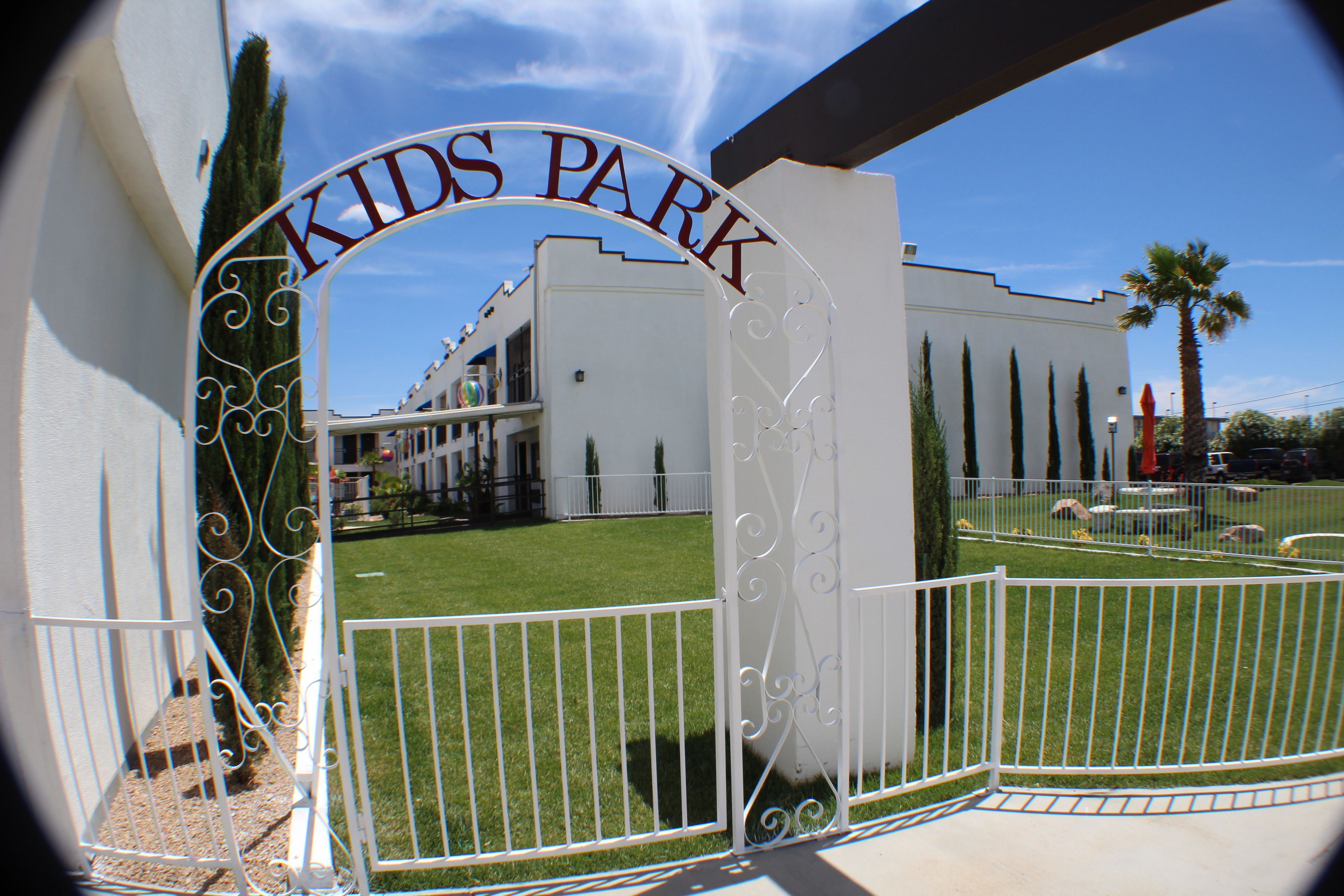 Una entrada con puerta a Kids Park, cielo despejado y un edificio blanco al fondo.