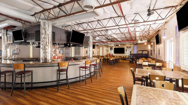 A spacious restaurant with a bar area, multiple seating options, and a high ceiling with exposed beams. - Ramada by Wyndham Kingman (Kingman)