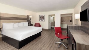 A hotel room with a large bed, a desk, a red chair, a TV, and a bathroom visible through an open door. - Ramada by Wyndham Kingman (Kingman)