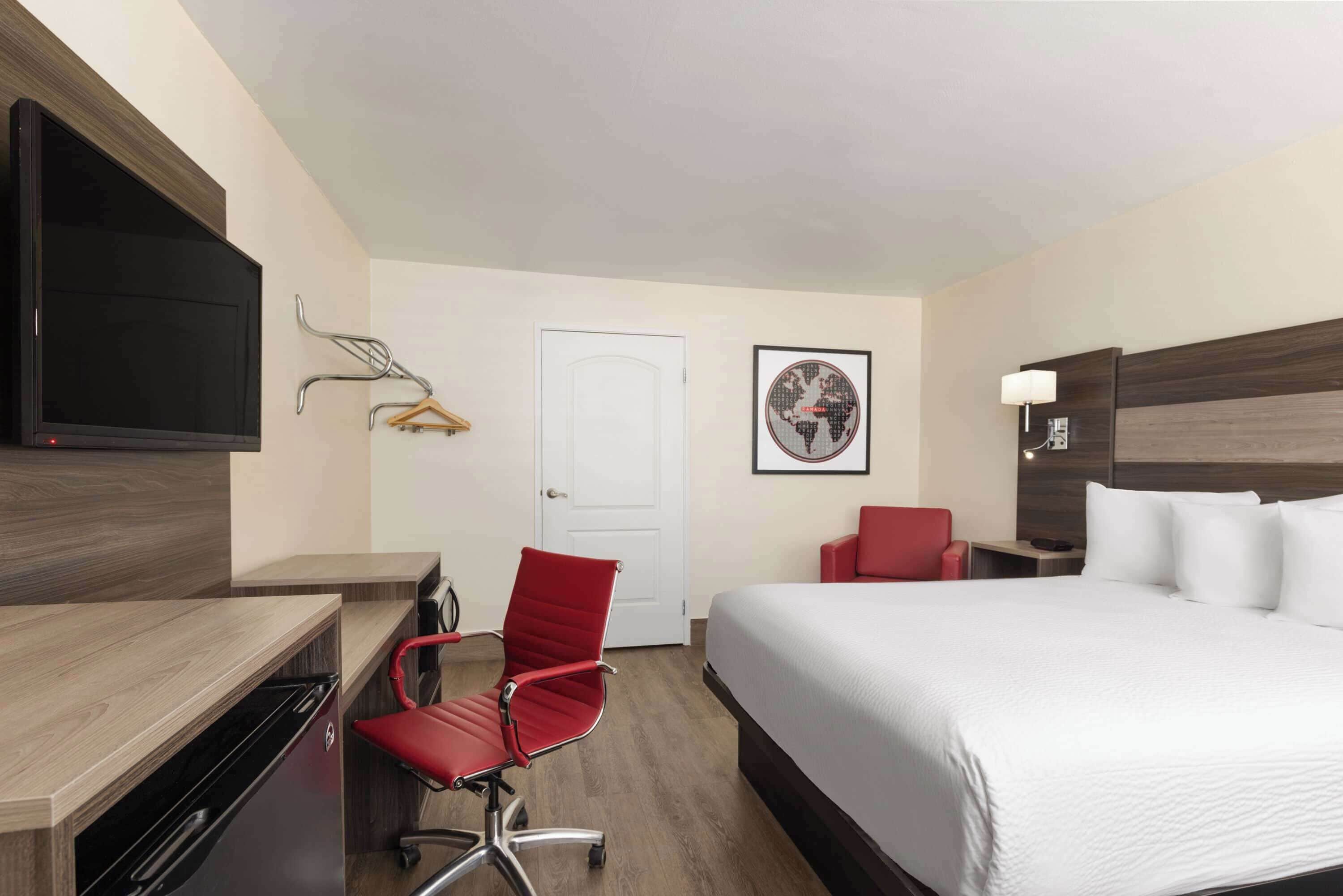 Habitación de hotel con cama, escritorio, silla, televisor, puerta y un cuadro en la pared.