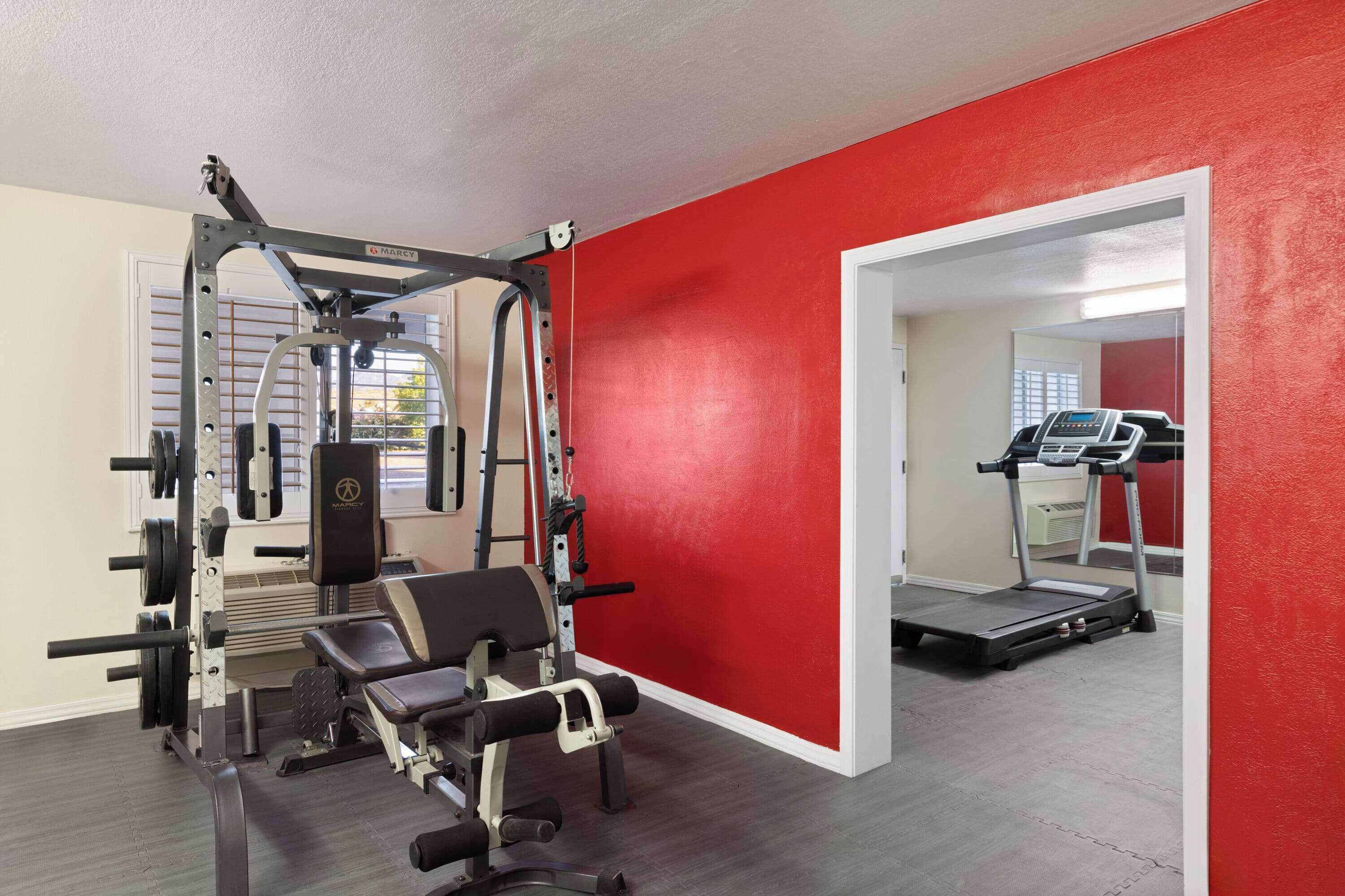Une salle de sport avec un mur rouge, un banc de développé couché et un tapis de course.