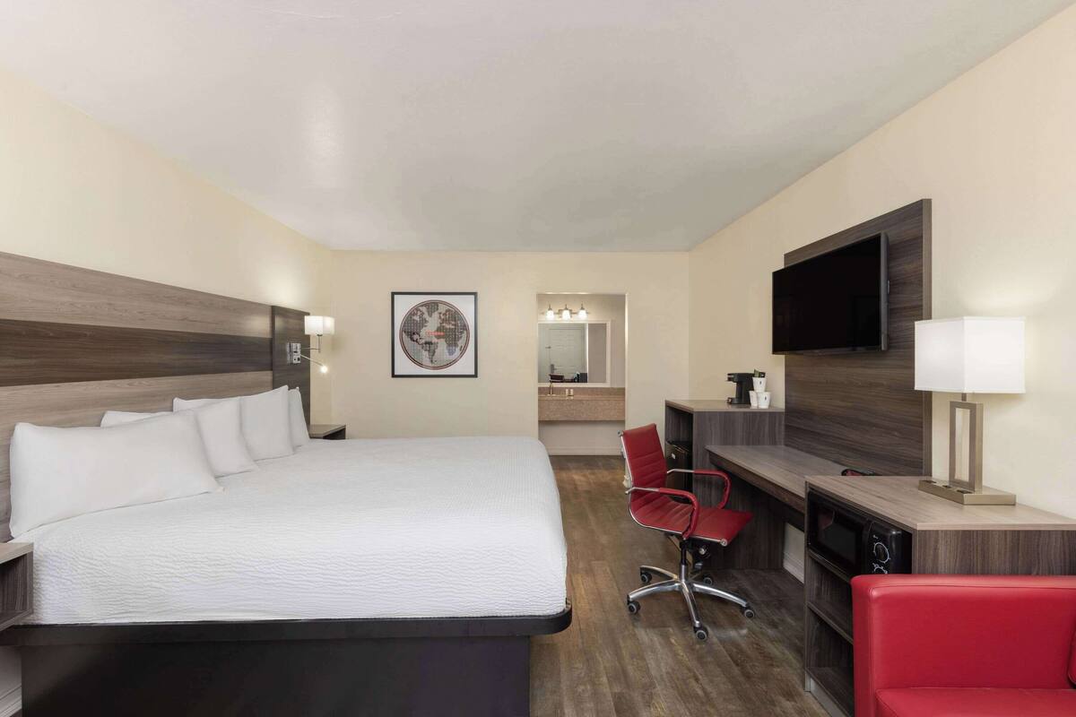 Ein Hotelzimmer mit einem großen Bett, einem Schreibtisch mit Fernseher, einem roten Sessel und einem Spiegel.