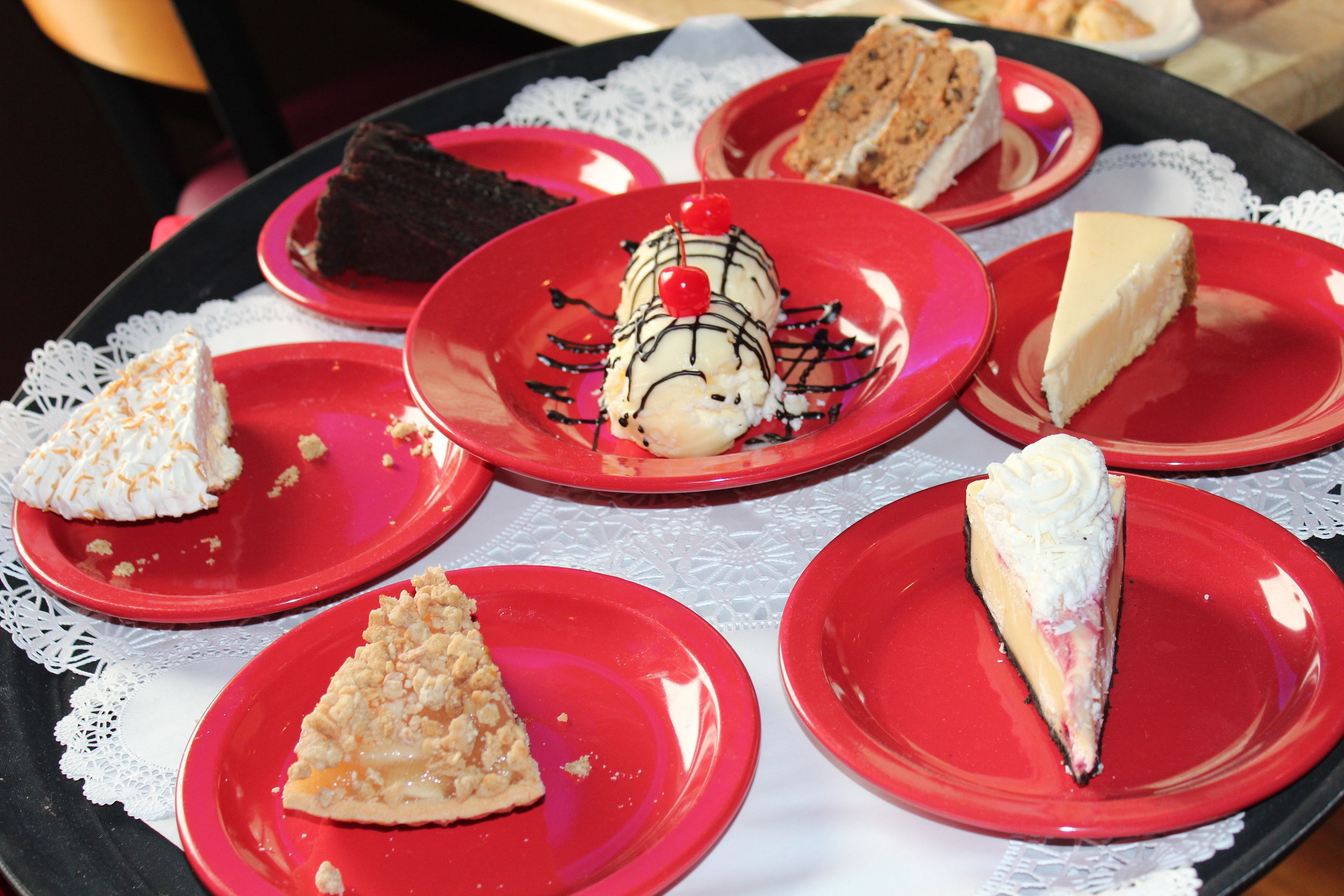 Een dienblad met diverse desserts op rode borden, waaronder ijs en taartpunten.