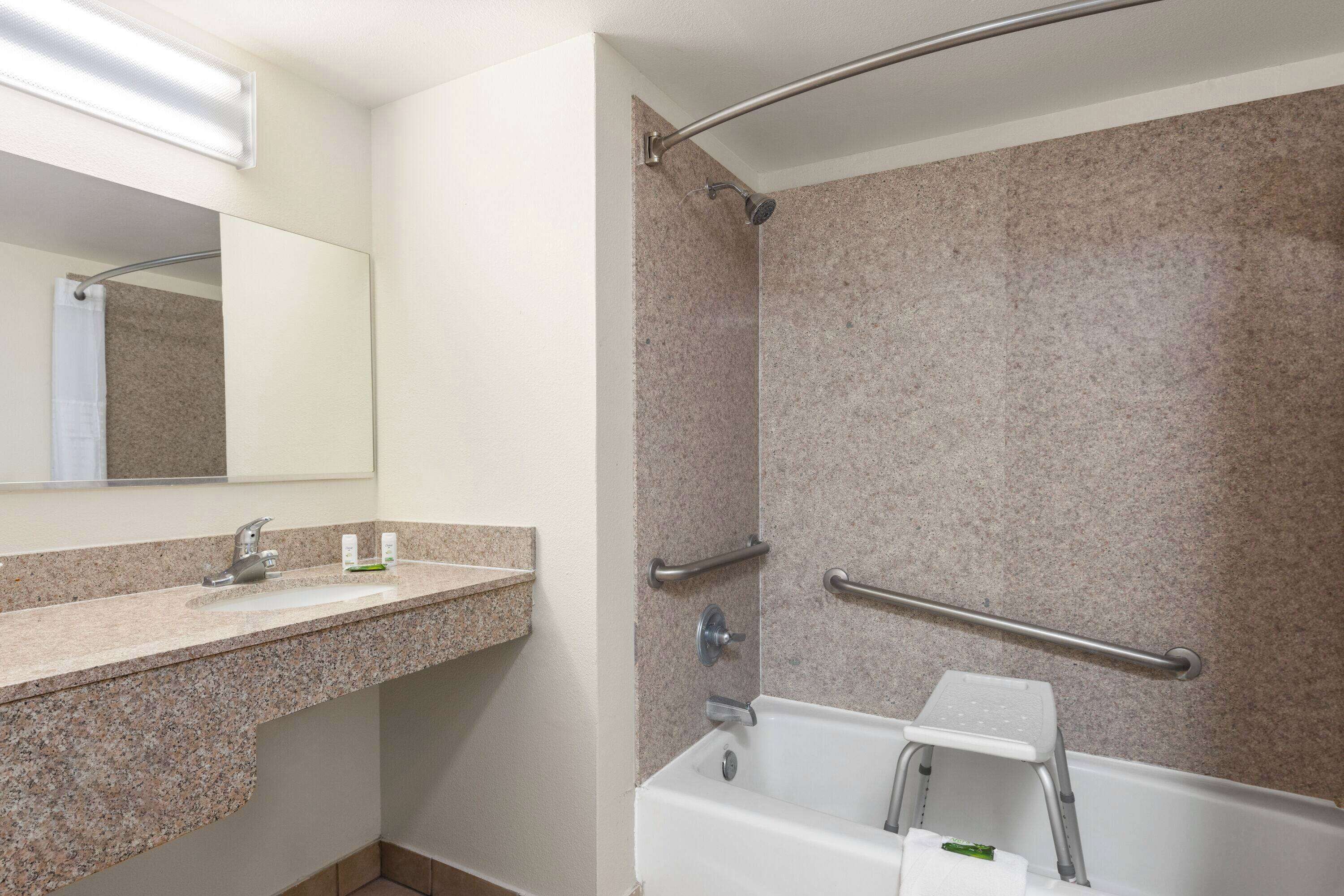 A bathroom with a granite countertop, a sink, a mirror, a shower with a glass door, and a grab bar.