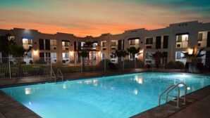 A swimming pool at dusk with a view of a multi-story building in the background. - Ramada by Wyndham Kingman (Kingman)