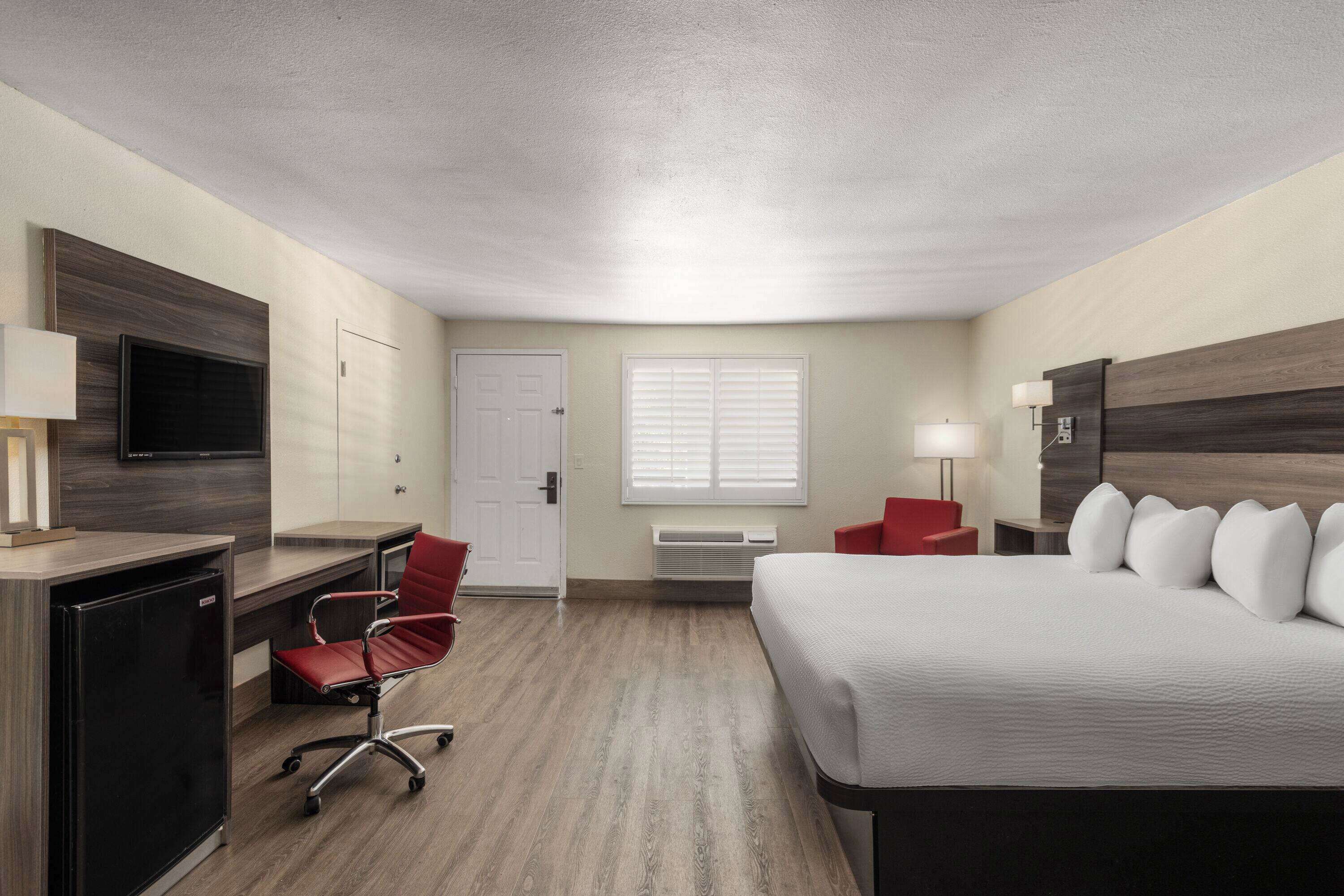 A hotel room with a bed, desk, chair, TV, and a window with blinds.