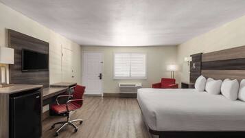A hotel room with a bed, desk, chair, TV, and a window with blinds.