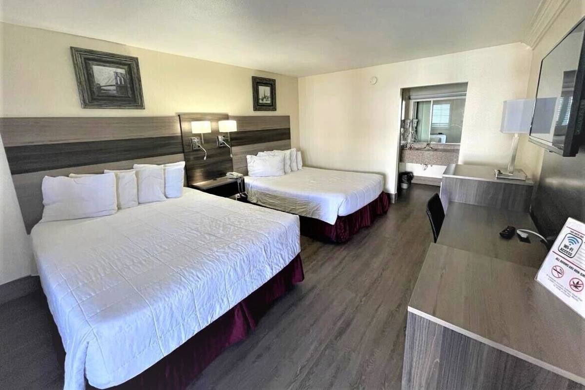 Ein Hotelzimmer mit zwei Betten, einem Schreibtisch, einem Fernseher und einem durchgegangenen Badezimmer.