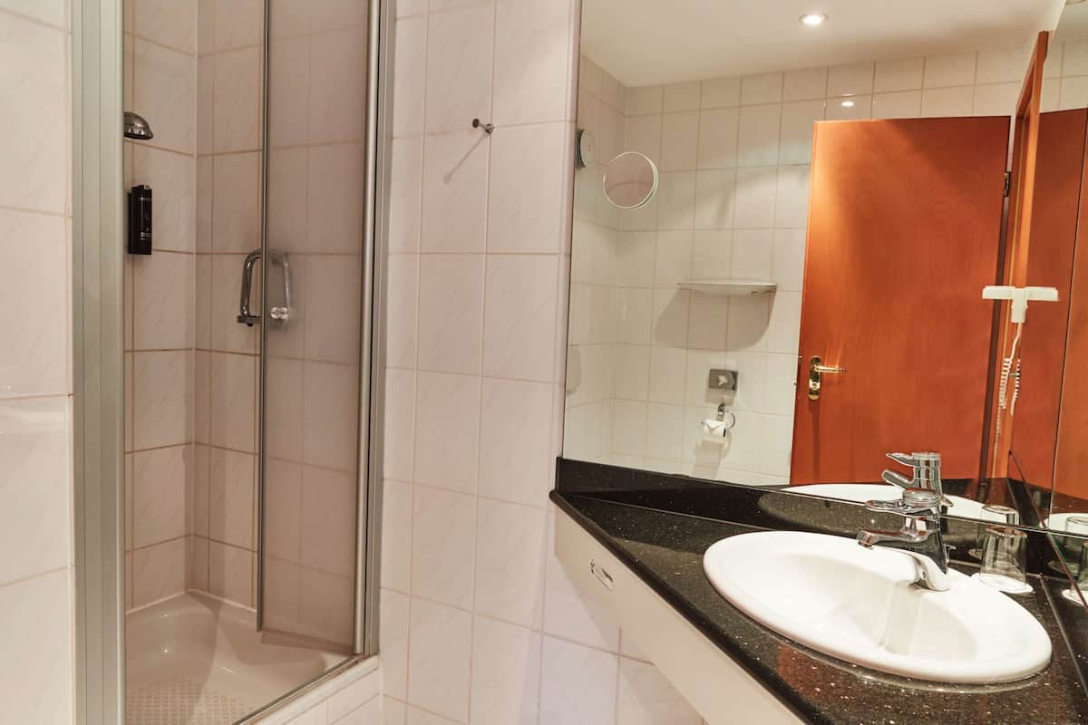 Une salle de bain moderne avec une douche à parois de verre, un lavabo blanc doté d’un plan de travail noir et une porte en bois.