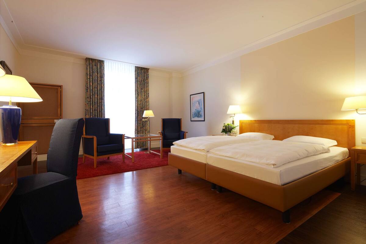 Une chambre d’hôtel avec un lit en bois, un bureau avec une lampe, une chaise et une petite table.