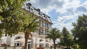 Een statig hotel met een klassiek gevelontwerp, meerdere balkons en buitenruimtes met parasols.