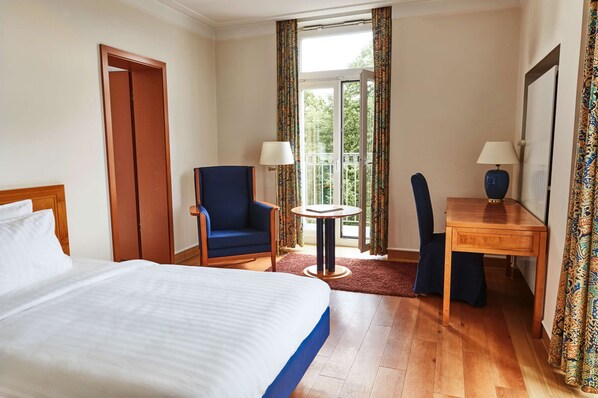A hotel room with a large bed, a desk with a chair, a small table, and a chair.