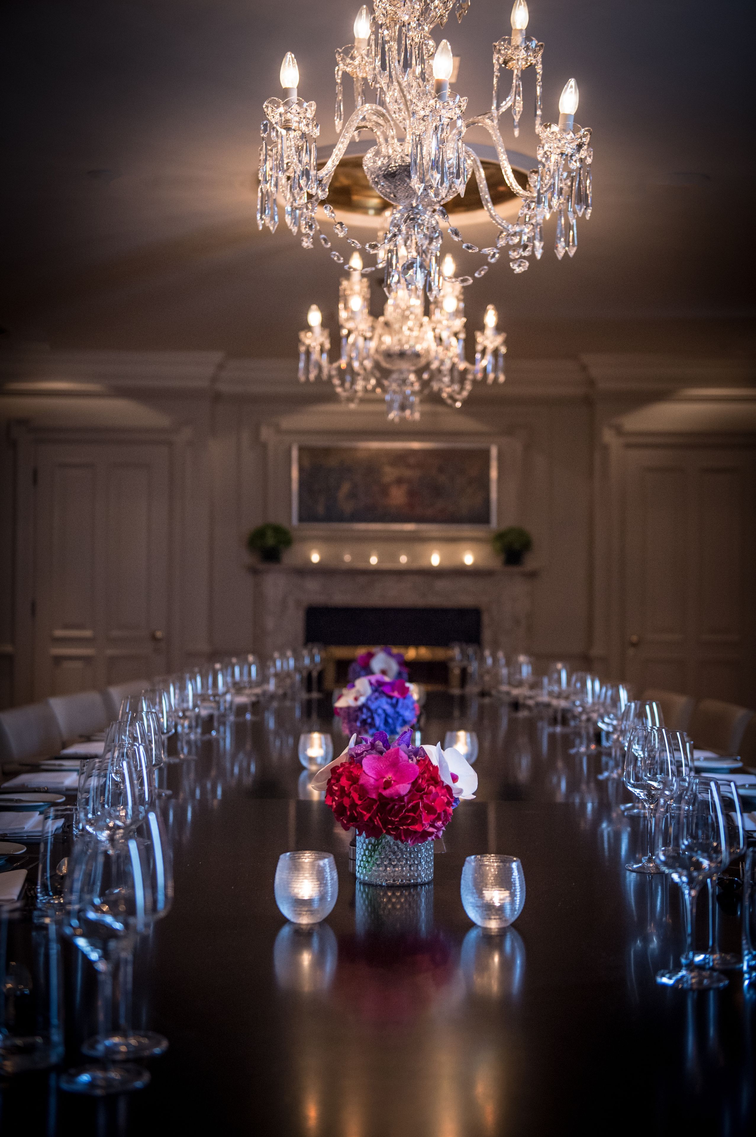Une longue table à manger entourée de chaises, un lustre et un vase rempli de fleurs.