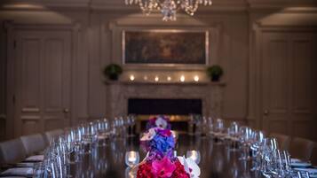 Une longue table à manger entourée de chaises, un lustre et un vase rempli de fleurs.