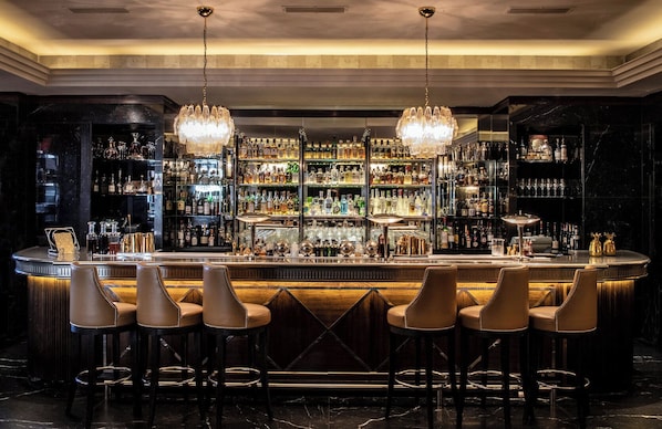 Uma área de bar com piso de mármore, banquetas e uma adega bem abastecida.