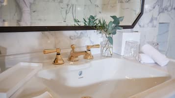 Ein Badezimmer mit einem weißen Marmorwaschbecken, goldenen Wasserhähnen und einem Spiegel darüber.