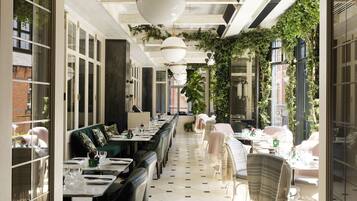 A long dining table with chairs, a tiled floor, and hanging plants.