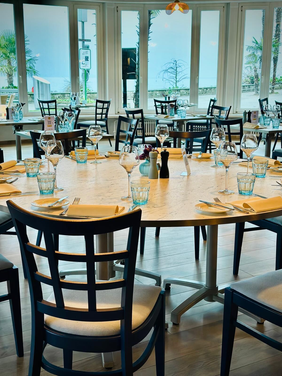 A restaurant with round tables set for dining, chairs, and wine glasses.