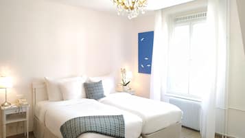 Ein Schlafzimmer mit einem großen Bett, einem Nachttisch mit Lampe, einem Wandbild und einem Fenster mit Vorhängen.