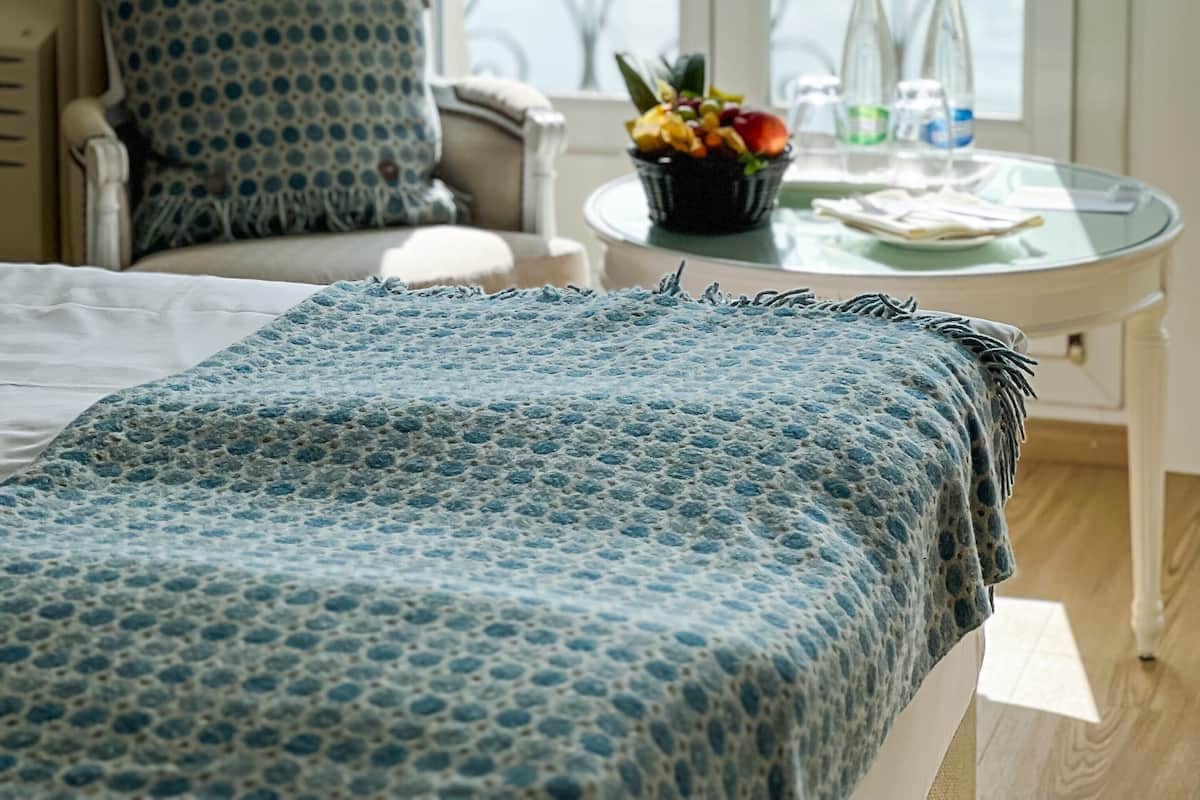 Habitación de hotel con cama, una silla, una mesita con frutero y vista al mar desde un balcón.