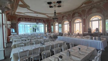 Una sala da banchetto con lunghe tavolate, sedie bianche e decorazioni elaborate al soffitto.
