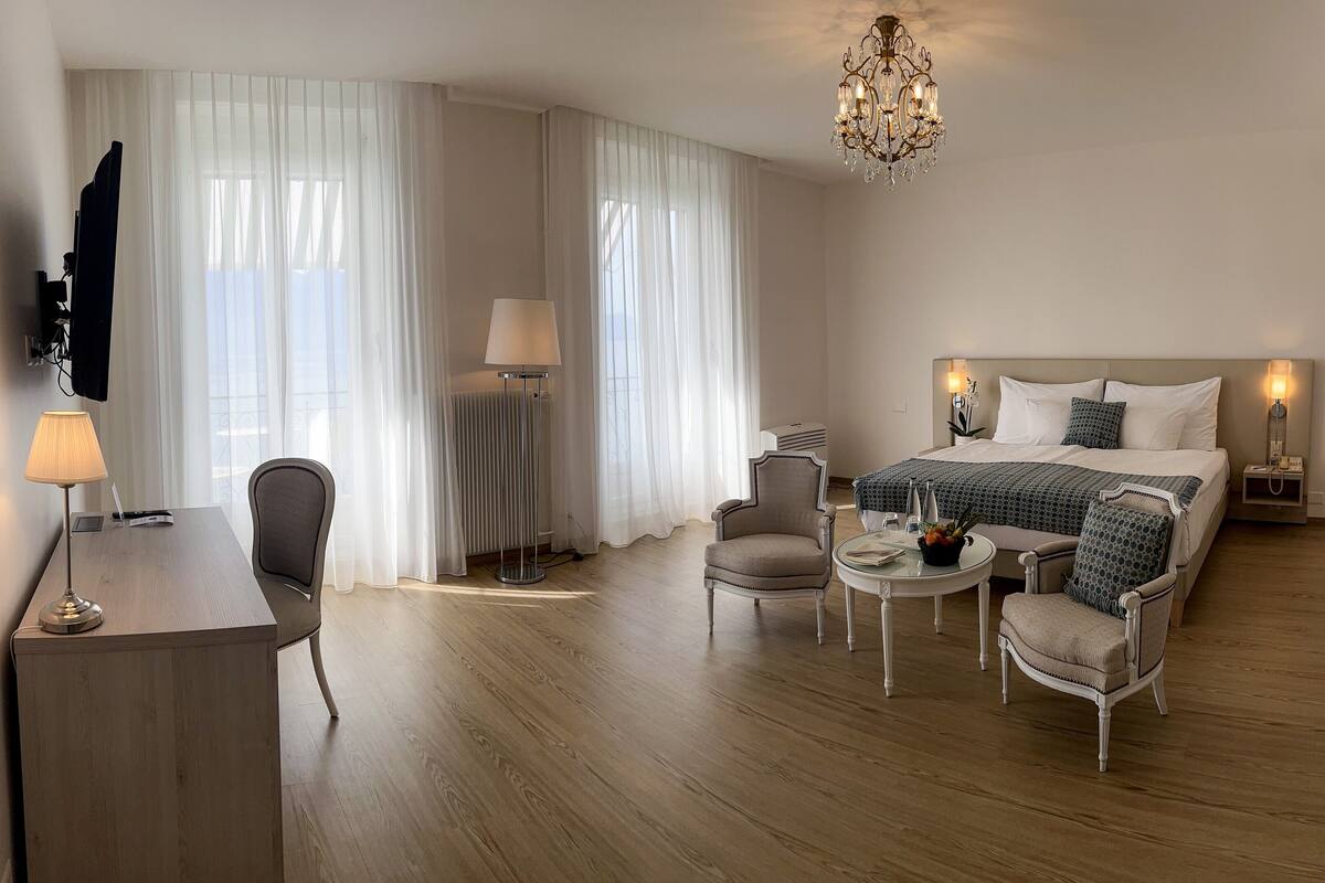 Una habitación de hotel con una cama, lámparas de noche, un escritorio con lámpara, una silla y una mesita.