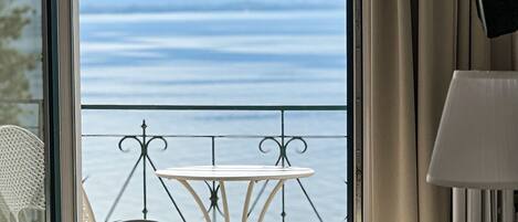A room with a view of the sea, a table with chairs, and a lamp.